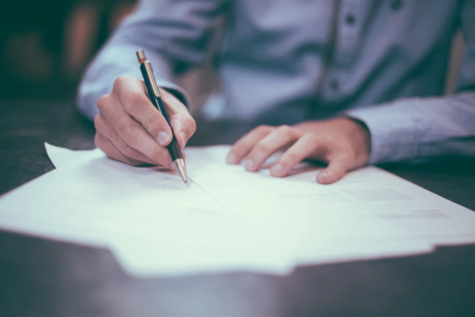 A hand signing a contract document at a desk